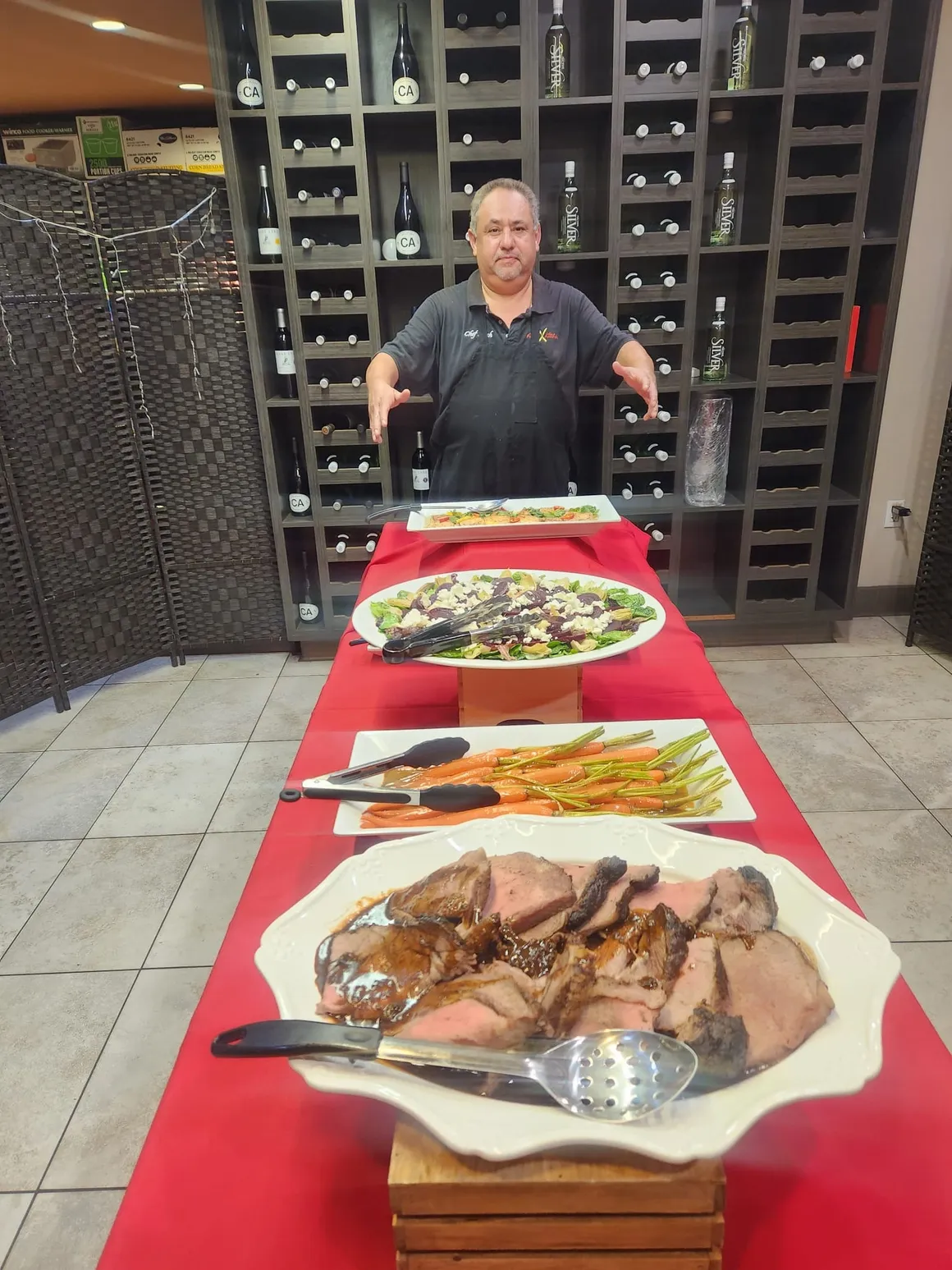 Chef Fitch with a roasted meat and salad spread on a red tablecloth